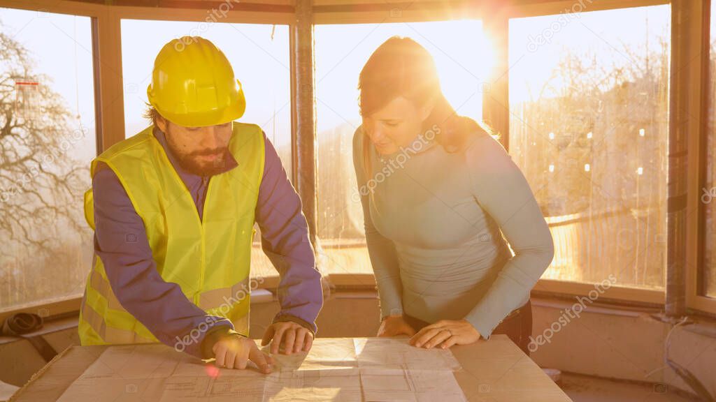 CLOSE UP: Young woman and contractor discuss the floor plans at golden sunset.
