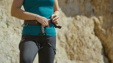 Dişi kaya tırmanıcısı, tırmanmadan önce kemerini beline bağlar.