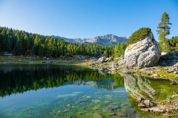 Küçük ahşap kulübe, Triglav Ulusal Parkı 'ndaki sakin göle bakıyor..