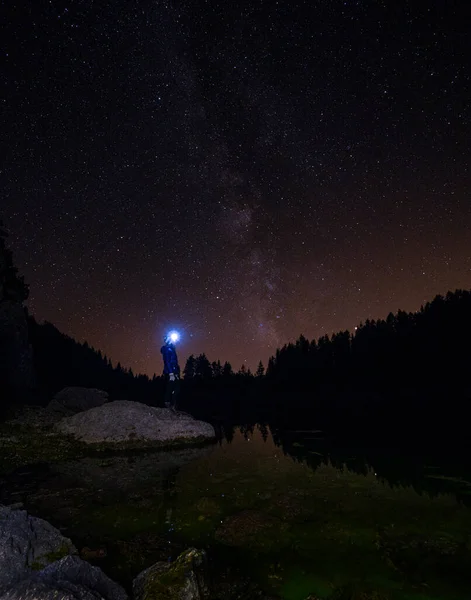 Female hiker wearing a headlamp stands on rock and observes the starry night sky