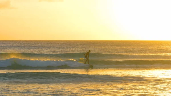 Un jeune surfeur surfe sur les vagues lors d'une soirée d'été pittoresque à la Barbade. — Photo