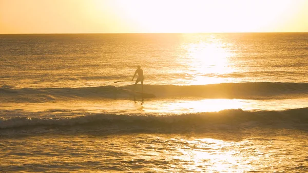 SILHOUETTE: Hombre de vacaciones en una tabla de surf y remos a lo largo de la costa. — Foto de Stock