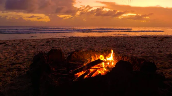 CLOSE UP: Small fire burns inside a fireplace on the sandy beach at sunset.