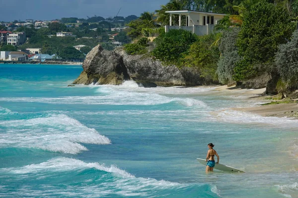 Giovane surfista femminile entra nell'acqua turchese dell'oceano con la sua tavola da surf. — Foto Stock