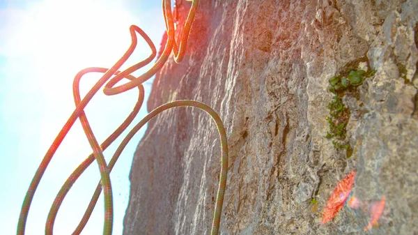 CLOSE UP, LENS FLARE: La cuerda verde y roja cae desde la cima de un imponente acantilado. — Foto de Stock