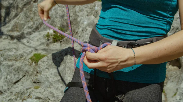 CLOSE UP: Woman fastens a rope onto the harness before climbing up a cliff. — Stock Photo, Image