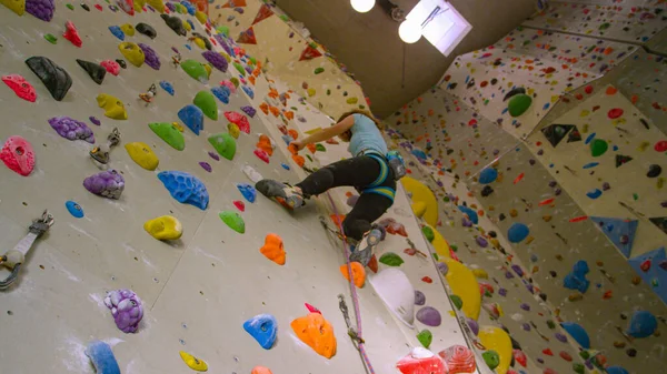 BOTTOM UP: Teenage climber climbs up an indoor wall filled with colorful holds. — Stock Photo, Image