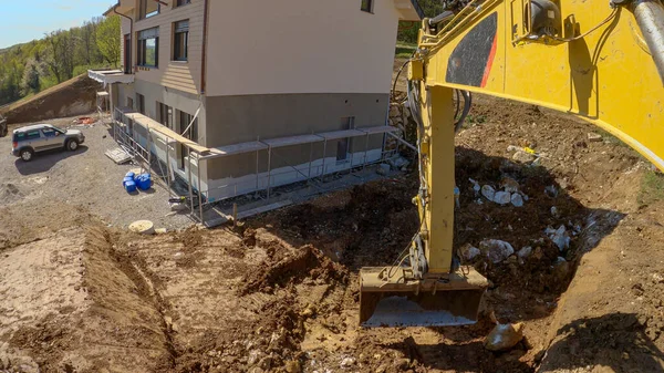 POV: Usando una excavadora Caterpillar para excavar tierra cerca de una casa sin terminar. — Foto de Stock