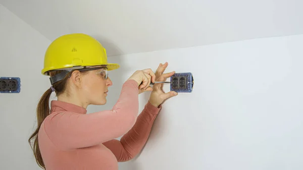 CLOSE UP: Woman screws screws into wall while installing electrical sockets