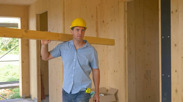 FECHAR UP: Carpinteiro feliz carregando uma prancha longa olha ao redor da casa CLT. — Fotografia de Stock