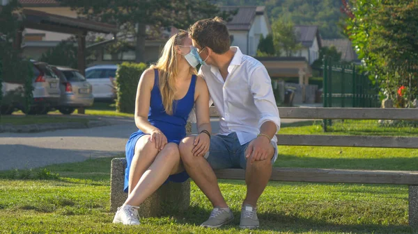 PORTRÄT: Kuscheliges Paar mit Gesichtsmasken küsst sich auf einer Parkbank — Stockfoto