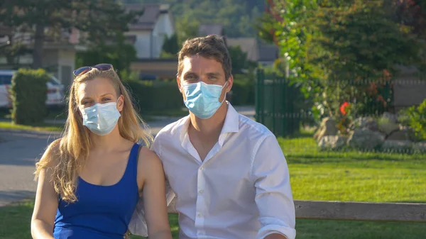 PORTRAIT Pareja usando mascarillas abrazos juntos mientras se sienta en un banco del parque —  Fotos de Stock