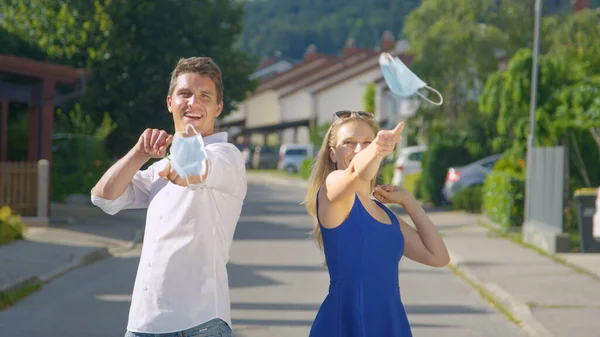 PORTRAIT: Cheerful man and woman take off their masks and flick them at camera. — Stock Photo, Image