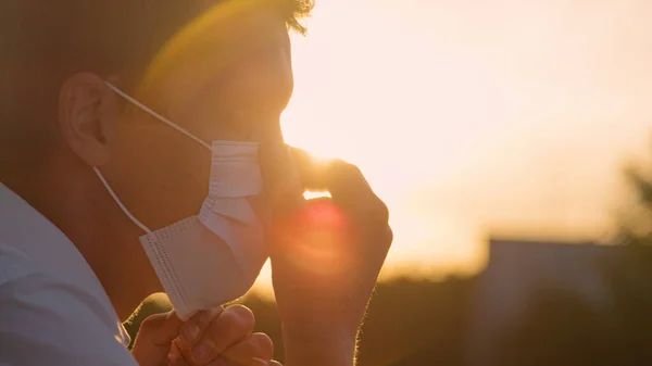 CERRAR: El hombre preocupado se pone una mascarilla mientras observa la puesta de sol dorada. —  Fotos de Stock