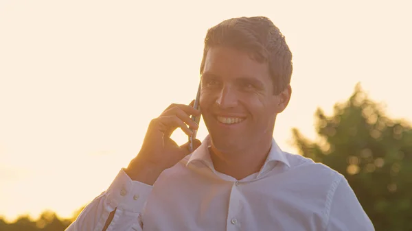 CLOSE UP: молодий бізнесмен посміхається під час розмови на мобільному телефоні на сході сонця . — стокове фото
