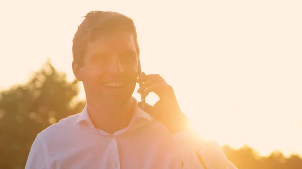 CLOSE UP: Man cheerfully talks on the phone on sunny evening after good meeting. — Stock Photo, Image