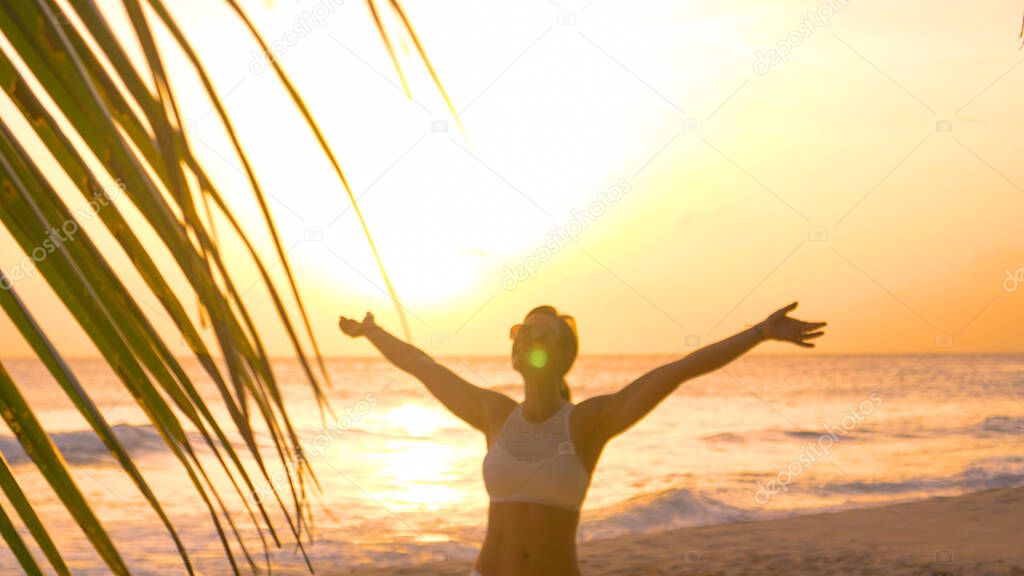 LENS FLARE, CLOSE UP: Smiling woman spins around a beach in the evening sunshine