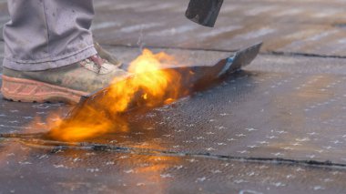 İşçi bir inşaat sahasına bitumen hidroizolasyon tabakası yerleştirir..
