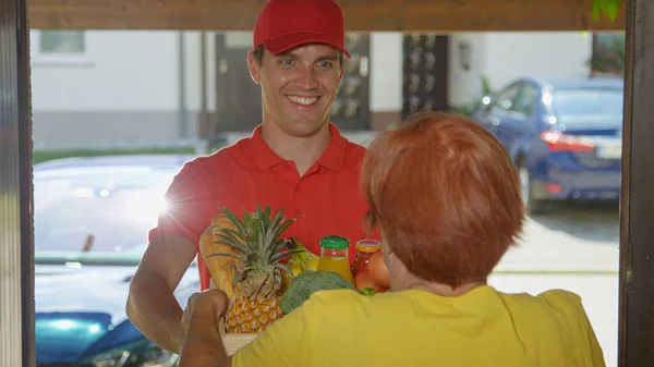 FERMER : Un coursier souriant portant une chemise rouge livre des produits d'épicerie à une aînée — Photo
