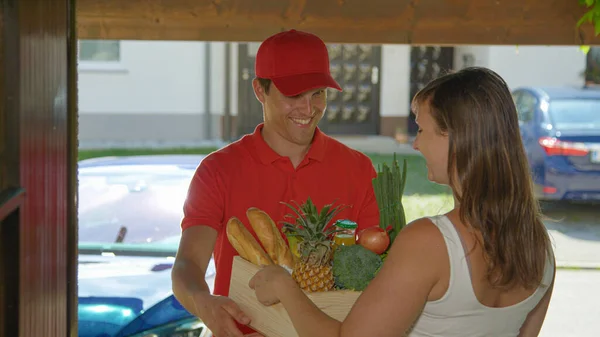 FERMER : Un coursier souriant portant une tenue rouge livre de l'épicerie à une jeune femme — Photo
