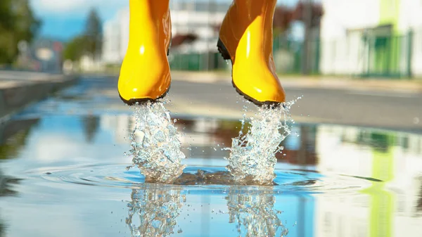 CLOSE UP: Непізнана жінка в жовтих дощових черевиках стрибає в калюжу . — стокове фото