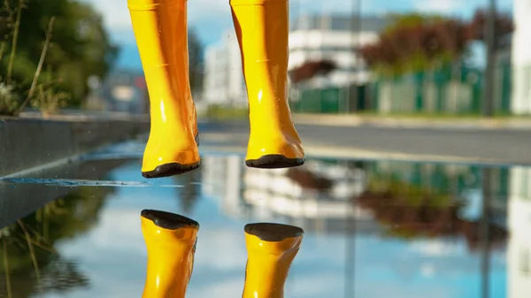 LOW ANGLE Cool shot of woman in yellow boots just before she jumps into a puddle — Stock Photo, Image