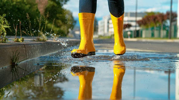 Щаслива жінка в жовтих дощових черевиках проходить через скляну калюжу . — стокове фото