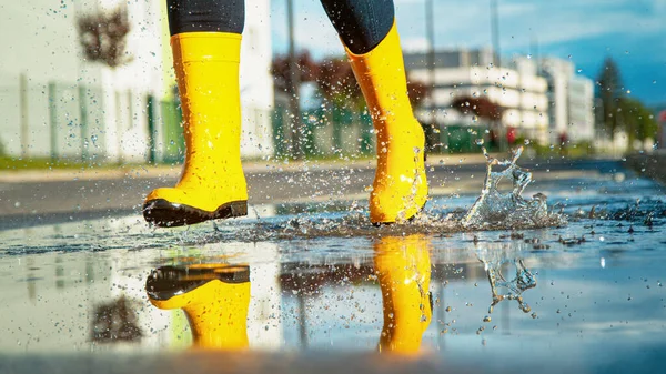 Жінка в жовтих дощових черевиках проходить через скляну калюжу . — стокове фото