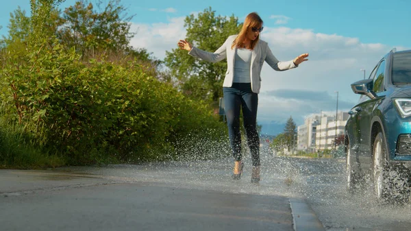LOW ANGLE: Woman is shocked as she gets splashed with water by careless driver
