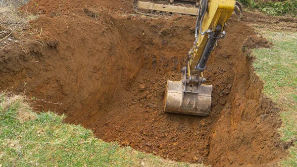 CERRAR: La excavadora amarilla cava un agujero profundo en medio de un prado. — Foto de Stock