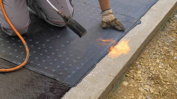 CLOSE UP: De aannemer gebruikt een brander om een bitumen vel op de grond te branden. — Stockfoto