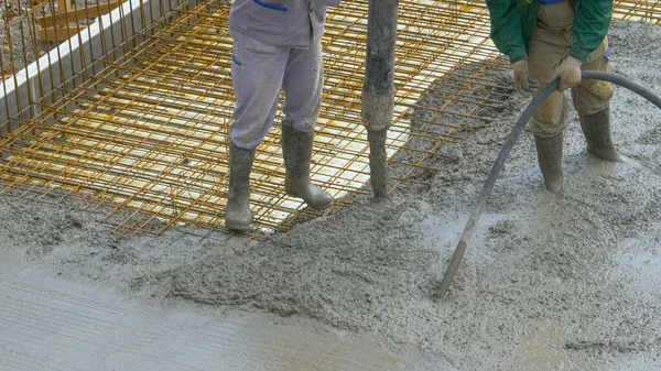 CHIUSURA: Un team irriconoscibile di lavoratori versa malta fresca sul cablaggio metallico. — Foto Stock