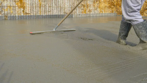 ÂNGULO BAIXO: Trabalhador irreconhecível usa uma ferramenta de nivelamento para espalhar o concreto molhado — Fotografia de Stock