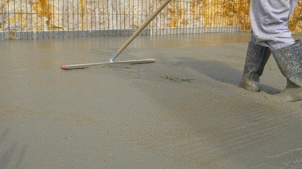 Низкий угол: Неузнаваемый работник использует выравнивающий инструмент для распыления мокрого бетона