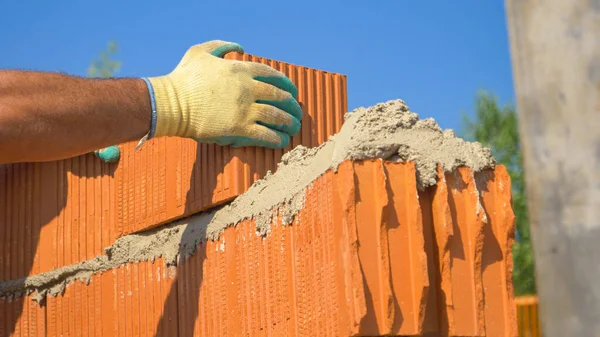 CHIUSURA: Costruttore irriconoscibile posa un nuovo mattone sulla cima di un muro in corso. — Foto Stock