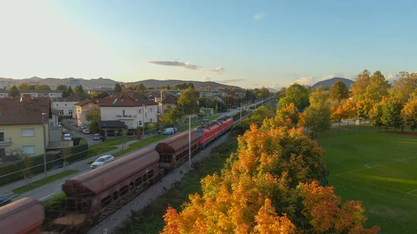 AERIAL: Industriellt tåg transporterar gods förbi en förort på hösten — Stockfoto