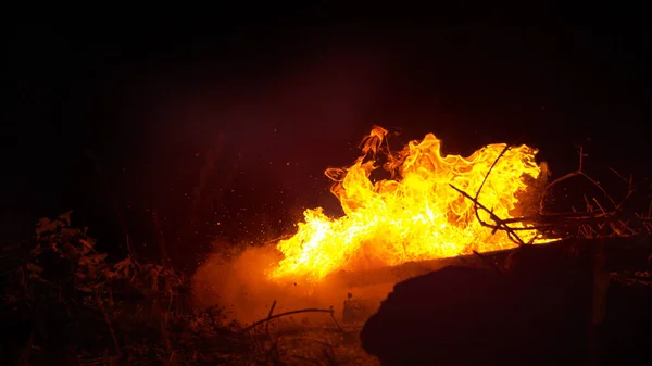 FECHAR UP: Um balde de combustível é espirrado em uma grande fogueira queimando à meia-noite — Fotografia de Stock