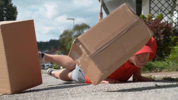 CLOSE UP: Uncoordinated delivery man falls to ground and drops cardboard boxes — Stock Photo, Image