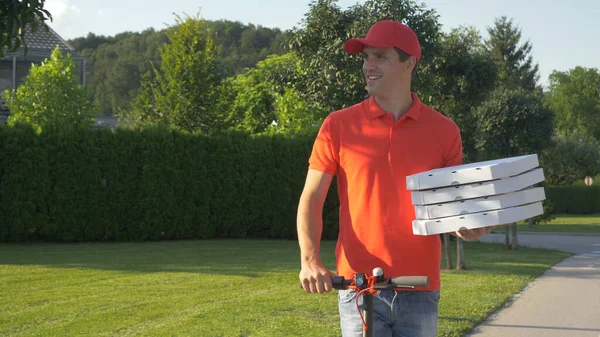 Kırmızı tişörtlü kurye e-scooterla pizza dağıtırken gülümsüyor. — Stok fotoğraf
