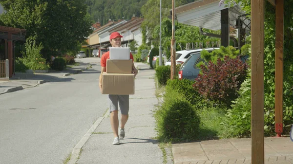 Young male courier leisurely strolls along the sidewalk carrying big packages. — Stock Photo, Image