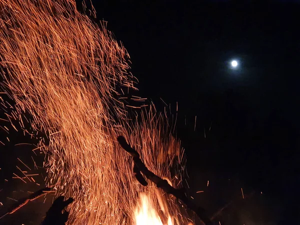Близко: Светящиеся оранжевые искры вылетают из пылающего огня в ночное небо. — стоковое фото