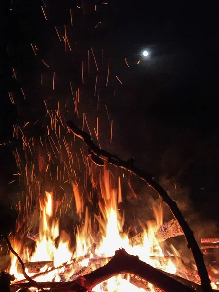 FERMER : La lune brille sur un feu de camp brûlant et apportant lumière et chaleur. — Photo