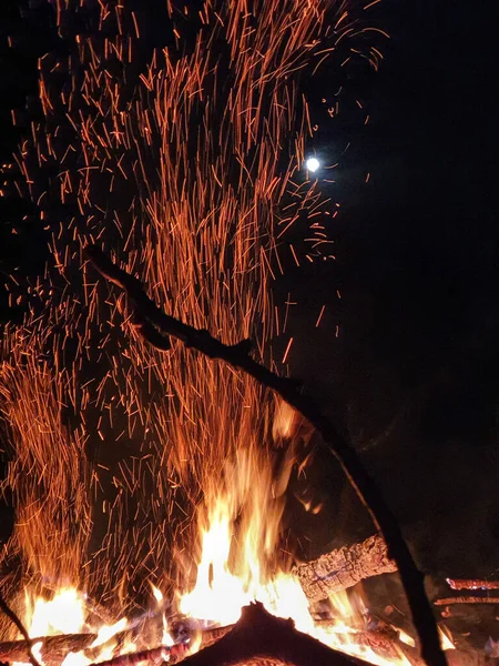 Светящиеся оранжевые искры вылетают из пылающего огня в ночное небо. — стоковое фото