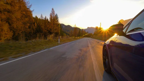 CLOSE UP: Cinematische opname van een blauwe auto rijden langs een schilderachtige weg bij zonsopgang. — Stockfoto