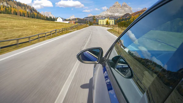 CERRAR: Brillante coche azul conduce a lo largo de camino vacío que conduce a la ciudad de Misurina. — Foto de Stock