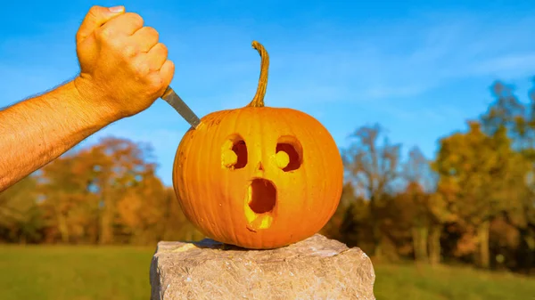 CLOS E UP: Calabaza de Halloween con una cara impactada es apuñalada con un cuchillo —  Fotos de Stock