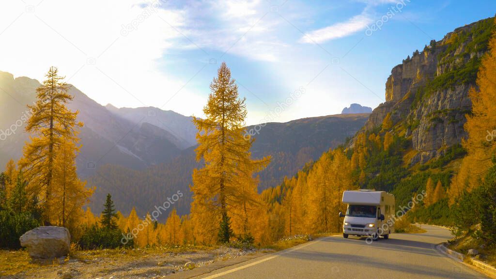White recreational vehicle drives up empty mountain road on a sunny fall day