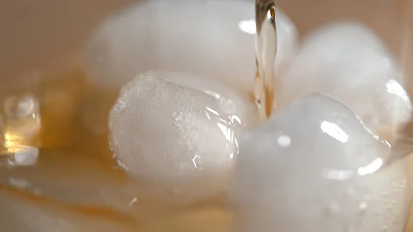 MACRO: Sabroso bourbon se vierte sobre el hielo derretido brillante sentado en un vaso. —  Fotos de Stock