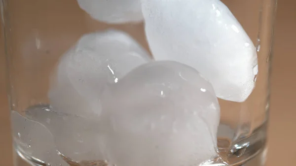 MACRO, DOF: Trozos redondos de hielo derretido rebotan alrededor de un vaso de licor vacío. —  Fotos de Stock