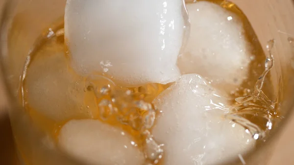 MACRO: Los cubitos de hielo fresco se dejan caer en un vaso lleno de whisky y hielo derretido —  Fotos de Stock